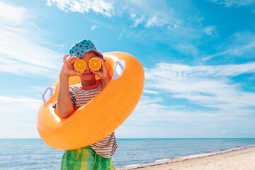 happy kid with fresh oranges and floatie on beach , concept of a healthy diet, vitamins, lifestyle