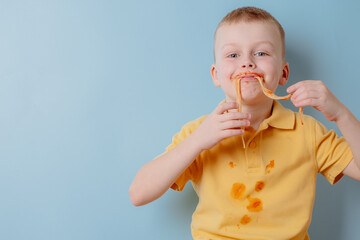 Portrait of a child eating spaghetti with hands. Boy stained with tomato sauce. isolated on blue background
