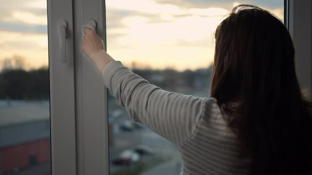brunette woman closes the window in the evening, moving camera