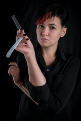 Obraz premium Half-length portrait of young adult barber woman on black background holding vintage straight razor, modern barber girl concept