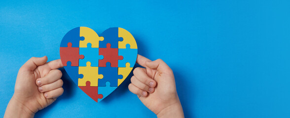 Autistic boy hands holding jigsaw puzzle heart shape. Autism spectrum disorder family support...