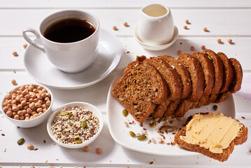 Wholegrain bread with chickpea paste on a white plate and a cup of coffee on the table. Healthy breakfast.