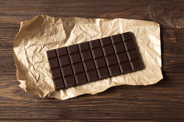 Bar of black bitter chocolate on wooden brown background, top view