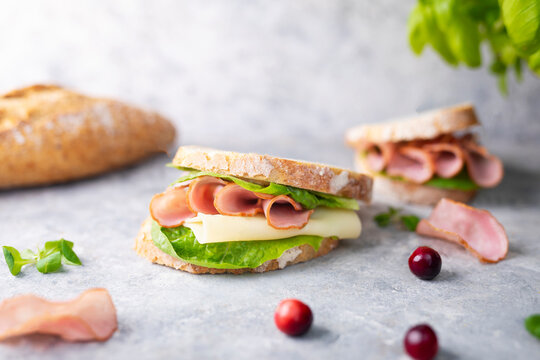 A sandwich made of crispy bread, dried, smoked sausage, cheddar, lettuce. Breakfast concept, composition with sliced homemade krakowska sausage on a stone worktop.