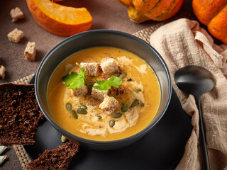 Pumpkin cream soup. Bowl with soup  and orange pumpkins on gray background. Healthy, vegetarian food. Lenten menu