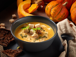 Pumpkin cream soup. Bowl with soup  and orange pumpkins on gray background. Healthy, vegetarian food. Lenten menu