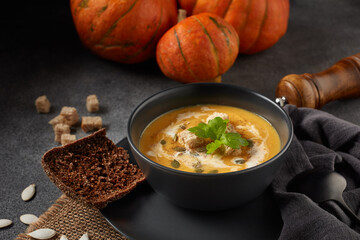 Pumpkin cream soup. Bowl with soup  and orange pumpkins on gray background. Healthy, vegetarian food. Lenten menu
