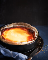 Homemade Basque burnt creamy cheesecake, New York style Cheese cake in a round baking tin, dark background, copy space, selective focus. Trendy dessert, home cooking, local food, San Sebastian, Spain.