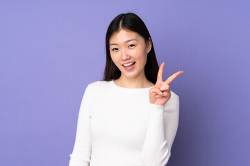 Young asian woman isolated on purple background smiling and showing victory sign