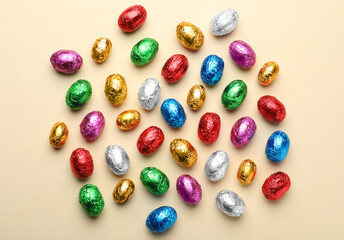 Fototapeta na wymiar Chocolate eggs wrapped in colorful foil on beige background, flat lay