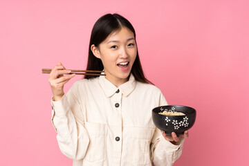 Young asian woman isolated on pink background holding a bowl of noodles with chopsticks