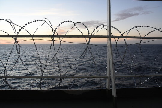 Barbed Wire Attached To The Ship Hull, Superstructure And Railings To Protect The Crew Against Piracy Attack In The Gulf Of Guinea In West Africa Sailing During Sunset.