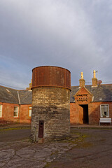 Fototapeta premium The Old Historical Iron Water Tower on a brick base in Fountain Square Auchmithie, with a small Doocot above the entrance of the central cottage,