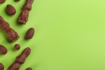 Flat lay composition with chocolate Easter bunnies and eggs on green background. Space for text
