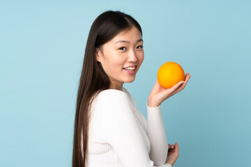 Young asian woman holding an orange over isolated blue background