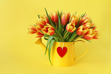 red and yellow tulips in tin can with wooden heart on yellow background