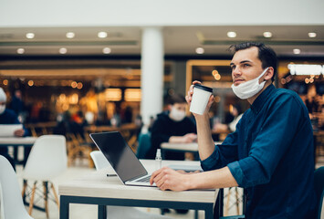 man in a protective mask sitting at a table in a cafe