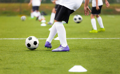 Fototapeta na wymiar Soccer Player Kicking Ball on Training. Group of Footballers Improving Skills on Practice Venue. Soccer Boy in Purple Cleats and White Soccer Jersey Kit