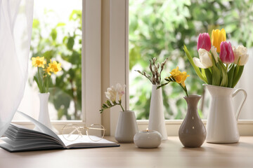 Different beautiful spring flowers, burning candle and book on window sill - Powered by Adobe