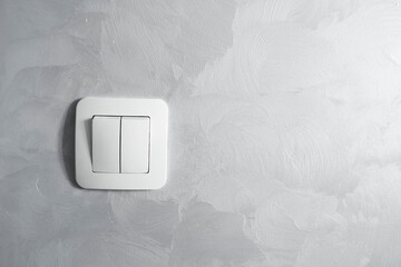 Light switch, a plastic mechanical switch of white color installed on a light gray wall.