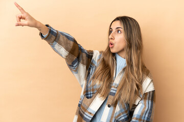 Young caucasian woman isolated on beige background pointing away