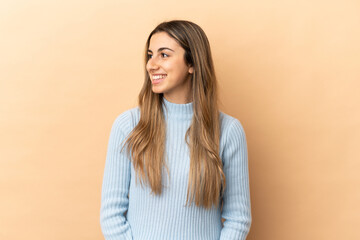 Young caucasian woman isolated on beige background looking side