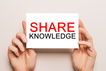 Female hands hold card paper with text SHARE KNOWLEDGE on a yellow background. Business and finance concept