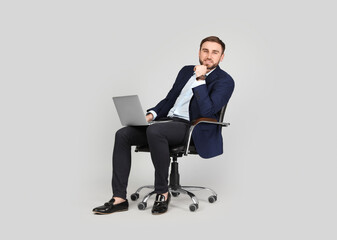 Young businessman with laptop sitting in comfortable office chair on grey background