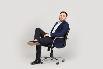 Young businessman sitting in comfortable office chair on grey background
