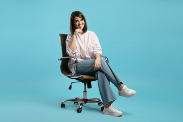 Young woman sitting in comfortable office chair on turquoise background