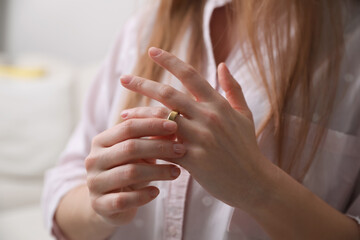 Woman taking off wedding ring indoors, closeup. Divorce concept