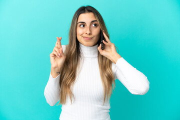 Young caucasian woman using mobile phone isolated on blue background with fingers crossing and wishing the best