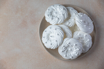 Plate with empty meringue nests, light stone background. Concept for a tasty sweet dessert. Top view.