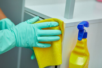 Bearded man cleaning home table surface with towel and gloves, disinfectant spray bottle