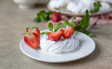 Mini meringue nest with fresh strawberries and mint on a plate, empty meringue nest and strawberries on concrete background.