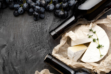 Obraz na płótnie Canvas Red wine bottle cheeses grapes. Vintage still life wine composition with aged cheese Camembert herbs, grapes. Restaurant dinner, wine tasting on dark concrete background.