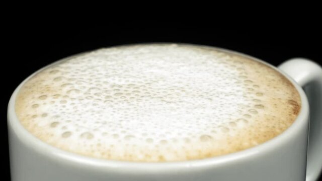 Sprinkling coffee foam with cinnamon powder in a cup on black background. Close-up. Slow motion