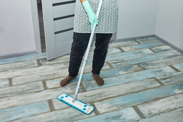 Bearded man in gloves with mop in hand cleaning floor in the house