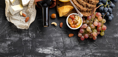 Food snacks Ingredients different cheeses grapes honey wine bread on dark concrete background. Long web banner. Wine and cheese composition. Mediterranean Kitchen gastronomy appetizer Red wine bottle