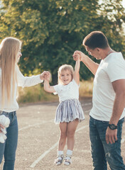 mom and dad raise their little daughter by the arms and she laughs