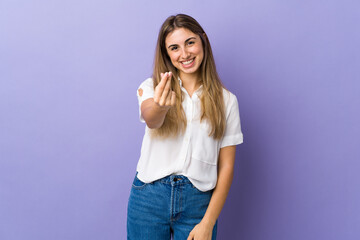 Young woman over isolated purple background making money gesture