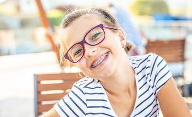 Young preteen girl in glasses wearing braces smiles at the camera on a summer day - 420429836