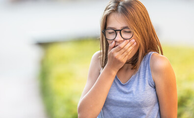 Teenager yawns outdoors holding hand in front of her mouth