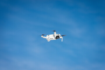 Small white drone flying on blue sky with clouds and copy space, photography.