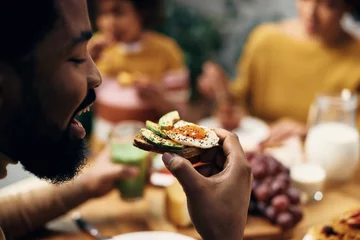 Poster Close-up van zwarte man die thuis een gezond broodje eet. © Drazen