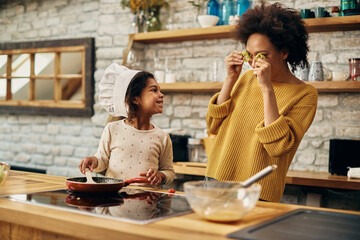 Happy black mother and daughter having fun with food while cooking in the kitchen.