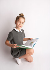 Attractive little girl in a strict school dress, stands on a white background with empty copy space, gestures with her hands, admires a happy expression on her face