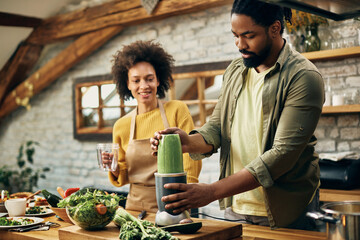 African American couple preparing green smoothie in the kitchen. - Powered by Adobe