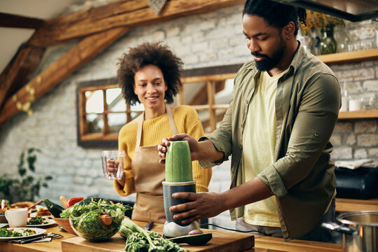 African American couple preparing green smoothie in the kitchen.