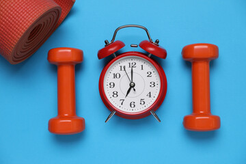 Alarm clock, dumbbells and yoga mat on light blue background, flat lay. Morning exercise